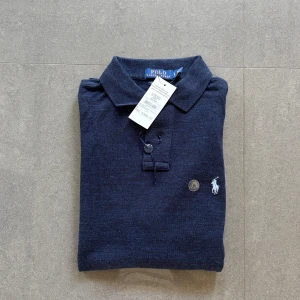 Ny grym pikétröja från Polo Ralph Lauren - Ny mörkblå pikétröja från Polo Ralph Lauren i custom slim fit.. Nypris 1000 kr. Ikoniska broderade loggan i vitt på bröstet. Perfekt för dig som gillar stilren och tidlös design.