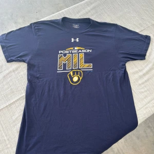Under Armour MLB Postseason t-shirt - Mörkblå t-shirt från Under Armour med Milwaukee Brewers MLB Postseason 2018-tryck i gult och vitt på bröstet. Klassisk rund hals, korta ärmar och loose fit. Perfekt för dig som älskar baseball och sportig stil.
