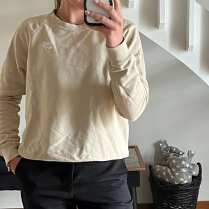 Beige Nike sweatshirt med broderad logga - Säljer en stilren beige sweatshirt från Nike med broderad vit logga på bröstet. Tröjan har rund halsringning och långa ärmar, perfekt för en avslappnad och sportig look. Använd fåtal gånger, nypris 549kr