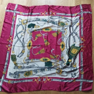 Silky scarf med ridinspirerat mönster - Snygg fyrkantig scarf i polyester med vinröd, vit, grön och guldfärgad design. Mönstret har detaljer som remmar, tofsar och spännen i en klassisk ridstil. Perfekt accessoar för att lyfta din outfit med lite lyxig känsla.