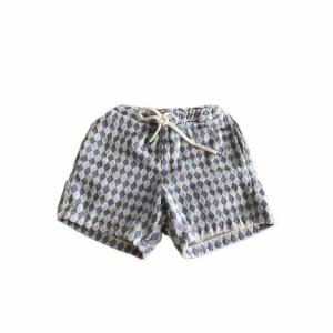 Blåvitrutiga shorts med snörning - Shorts med blåvitt rutmönster och bekväm snörning i midjan. Tillverkade i mjukt frottématerial som ger en avslappnad vibe. Perfekta för varma dagar när du vill ha något både snyggt och chill.