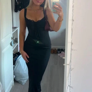 Svart långklänning med spetsdetalj - Supersnygg svart långklänning med breda axelband och figurnära passform. Klänningen har spetsdetaljer vid bysten och en liten snörning framtill som ger en extra touch. Tryck på KÖP NU så postar jag så snabbt som möjligt!! 🩷🩷