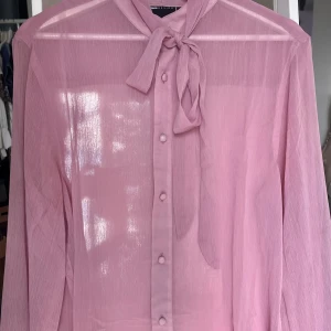 Rosa transparent blus från ASOS DESIGN - Säljer en superfin rosa transparent blus från ASOS DESIGN. Blusen har långa ärmar, knappar framtill och en snygg knyt-detalj i halsen. Materialet är lätt och luftigt, perfekt för att skapa en cool och trendig look. Aldrig använd pga för kort i ärmarna på mig som är 185cm. 