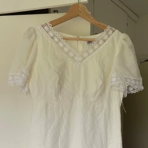 Retro Vit långklänning - Romantisk vit långklänning med v-ringning och fina spetsdetaljer vid halsringning, ärmslut och nederkant. Klänningen har korta puffärmar och en mjukt böljande siluett. Perfekt för dig som gillar en klassisk och feminin stil. Vintage från secondhand 