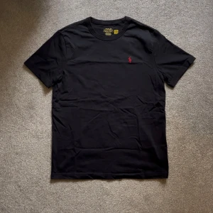 Ralph Lauren T-shirt - Säljer en snygg svart T-shirt med rött märke från Ralph Lauren, Skick: 10/10 knappt använd. Storlek S, hör gärna av er vid frågor, Mvh