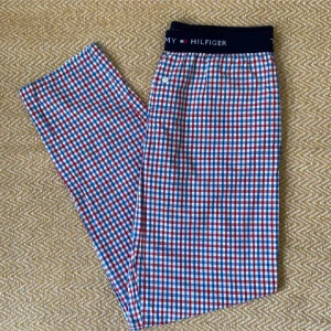 Rutiga pyjamasbyxor Tommy Hilfiger blå/röd - Snygga rutiga byxor från Tommy Hilfiger i blått, rött och vitt. Mjukt bomullsmaterial och elastisk midja med logotyp. Perfekta för chill dagar hemma eller när du vill ha en avslappnad look.