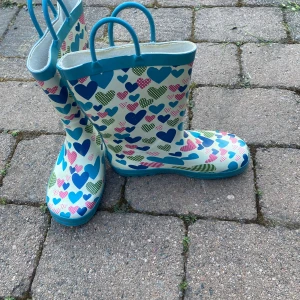 Färgglada stövlar med hjärtmönster - Snygga gummistövlar med blå kant och handtag, täckta av hjärtan i blått, rosa och grönt. Perfekta för regniga dagar och festivaler. Stövlarna har rund tå och platt sula för bekväm användning.
