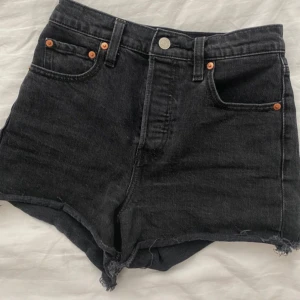 Svarta Levi's jeansshorts - Snygga svarta jeansshorts från Levi's. Klassisk femficksmodell med Levi's läderpatch bak och röda logotag. Perfekta för sommaren och ger en cool vibe till din outfit.