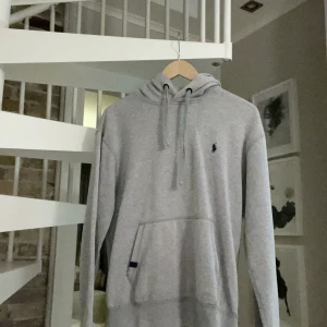 Grå hoodie från Polo Ralph Lauren - Snygg ljusgrå hoodie från Polo Ralph Lauren med klassisk broderad logga på bröstet. Tröjan har huva med snörning, känguruficka och långa ärmar. Perfekt för en chill och stilren look. Lite små defekter på den som lite fläckar men syns knappt de är en äldre model. Går att pruta 💸💸