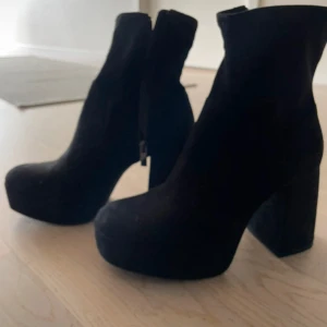 Svarta mocka stövletter med platå - Snygga svarta stövletter i mocka med hög klack och rejäl platåsula. Skorna har rund tå och dragkedja på sidan för enkel påtagning. Perfekta för dig som vill ha en edgy och trendig look.