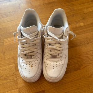 Nike Air Force 1 vita sneakers - Klassiska Nike Air Force 1 sneakers i helvitt skinn med perforerad tå och rund tå. Snygg och tidlös modell med snörning och platt sula. Perfekta för dig som gillar streetstyle och vill ha en ikonisk sneaker i garderoben. Fläck finns som ej går bort, se bild. Knappt använda
