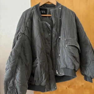 Grå bomberjacka från Zara - Säljer en oversized bomberjacka från Zara i mörkgrått. Jackan har ribbade muddar, dragkedja och tryckknappar framtill samt fickor.