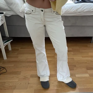 Vita bootcut jeans med detaljer - Säljer ett par vita bootcut jeans med snygga detaljer och nitar vid fickorna fram och bak. Jeansen har normal passform och är tillverkade i ett klassiskt jeanstyg. Perfekta för dig som vill sticka ut lite extra!