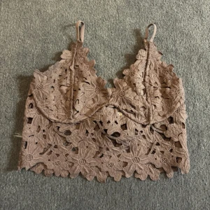 Lila blommig spets bralette - Säljer en Lila bralette med blommigt spetsmönster och tunna axelband. Toppen är croppad och har fina broderade blommor över hela tyget. Perfekt för sommaren eller som ett snyggt lager under en skjorta.