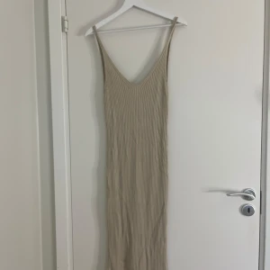 Beige ribbad långklänning med smala axelband - Säljer en beige långklänning med smala axelband och v-ringning både fram och bak. Små fläckar som inte syns alls, storlek L men passar som en M men också stretchig! 