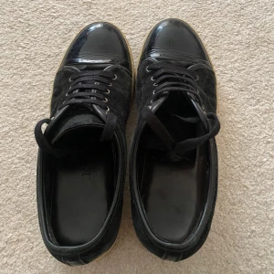 Svarta lanvin skor - Snygga svarta sneakers med snörning, lackad tå och sula i beige. Ovandelen är i mocka och tån är i blankt material som ger en cool kontrast. Perfekta för dig som vill ha en stilren men ändå unik look. Bara lite smutsiga där på sista bilden. Har inte orkat tvätta bort det men det är enkelt att göra. Säljs då jag har för många skor. Uk9