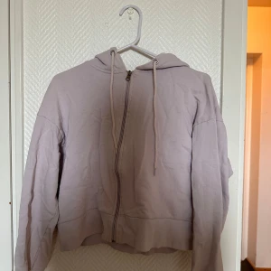 Ljuslila hoodie med dragkedja från 157 - Säljer en ljuslila hoodie från 157 i storlek XS. Tröjan har dragkedja framtill, huva med snören och är croppad i modellen. Perfekt för en avslappnad stil och enkel att matcha med jeans eller mjukisbyxor.