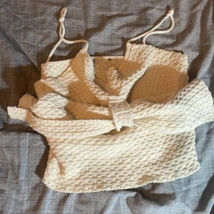 Beige croppad linnetopp med knytband - Säljer en söt beige croppad linnetopp med tunna axelband som knyts. Toppen har en strukturerad yta och är perfekt för varma dagar. Enkel och stilren design som passar till mycket.