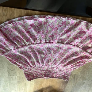 Blommig volang kjol från Gina Tricot - Supersöt kortkjol från Gina Tricot med blommigt mönster i rosa, vitt och grönt. Kjolen har smockad midja som ger en bekväm och stretchig passform. Perfekt för dig som gillar romantisk och färgglad stil. Den har gått sönder lite vid sömnen som man ser på bilden men de är inget man märker o de är inget som jag tycker gör något.