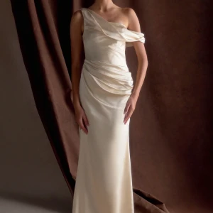 Champagnefärgad långklänning med oneshoulder - Elegant långklänning i champagnefärgat satinmaterial med draperad design och oneshoulder-skärning. Klänningen har en vacker omlottkänsla vid midjan och axeln, vilket ger en lyxig och sofistikerad look. Den är köpt från Meshki för 2300 inklusive tull men säljer den för 1500kr❣️ den är sprillans ny, endast testad. 