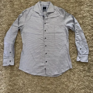 Ljusblå slim fit skjorta från Profuomo - Säljer en ljusblå och vit mönstrad skjorta från Profuomo i slim fit-modell. Skjortan har långa ärmar, knappar framtill och klassisk krage. Perfekt för dig som gillar stilrena detaljer och bekvämt material.