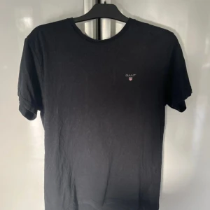 Svart t-shirt från GANT - Säljer en svart t-shirt från GANT i storlek L. T-shirten har rund halsringning och liten GANT-logga på bröstet. Tillverkad i 100% bomull för en skön och klassisk känsla. Perfekt till jeans eller shorts.