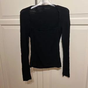 Svart långärmad topp - En stilren svart långärmad topp med tight passform och fyrkantig ringning. Perfekt att styla till olika outfits och enkel att matcha med både jeans och kjol. I strl S