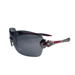 Oakley compulsive  solglasögon med röda skalmar - Snygga sportiga solglasögon från Oakley med svarta, stora, välvda linser och röda skalmar. Lätta bågar utan ram runt glasen och med Oakleys logga på sidan. Perfekta för en aktiv livsstil och ger ett coolt intryck.