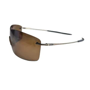  Oakley Nanowire 3.0 solglasögon  - Snygga solglasögon från Oakley med stora, bruna linser och tunna metallbågar. Glasögonen har en sportig och futuristisk design med näskuddar i silikon och minimalistiska skalmar. Perfekta för dig som gillar stilrena accessoarer.