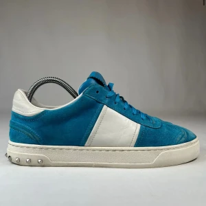 Valentino sneakers i blå mocka och vitt skinn - Säljer ett par snygga Valentino sneakers i blå mocka med vita skinnpaneler och vit sula. Skorna har silverfärgade nitar på hälen och klassisk låg profil. Perfekta för dig som gillar stilrena men ändå unika sneakers.