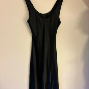Svart långklänning från BikBok - En stilren svart långklänning från BikBok i slätt material. Klänningen är ärmlös med rundad halsringning och har en figurnära passform. Perfekt för dig som gillar minimalistisk och tidlös stil.