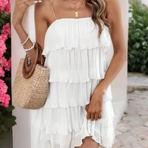 Vit volangklänning med tunna axelband - Superfin vit kortklänning med flera lager volanger och tunna axelband. Klänningen har plisserat tyg och en luftig känsla, perfekt för varma dagar. Passar dig som gillar en romantisk och somrig stil. Perfekt även till studenten!💛OBS: Lånade bilder från hemsidan, aldrig använd.