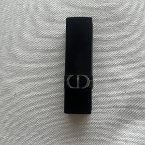 Rouge Dior läppstift 866 - Rouge Dior läppstift i färgen 866, med en djup röd nyans. Hylsan är svart med silverfärgad Dior-logga och har en lyxig känsla. Perfekt för dig som vill ha en klassisk och elegant look. Kommer utan förpackning, oanvänd och otestad, om du köper fler av dessa läppstift kan jag tänka mig bättre pris. Rensning inför flytt. Vissa märken på själva skalet på läppstiftet då jag förvarat alla i samma låda 