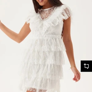 Studentklänning med spets - Superfin vit spetsklänning med volangdetaljer och kort ärm. Klänningen har flera lager med volanger och en v-ringad spets upptill. Perfekt till studenten