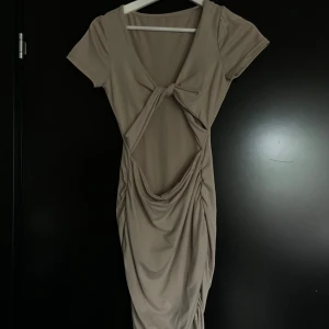 Beige kortklänning med twist och cut-out - Trendig beige kortklänning med twistad detalj framtill och snygg cut-out under bysten. Klänningen har korta ärmar och figurnära passform, perfekt för dig som vill sticka ut. Mjuk och stretchig känsla.