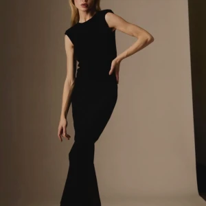 Svart ribbad långklänning från Ávora - Säljer en svart ribbad långklänning från Ávora med ärmlös design och öppen rygg. Klänningen har en tight passform och rund halsringning. 