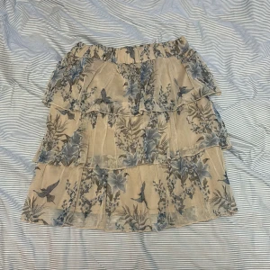 Blommig volangkjol från Trendyol - Supersöt kort kjol från Trendyol med flera lager volanger och blommigt mönster i blått och beige. Kjolen har elastisk midja och ett luftigt, flowy material som passar perfekt till varmare dagar.  Tror den hade blivit jätte snygg om man klipper den lite om man gillar kortare kjolar annars är den jätte fin som den är också 