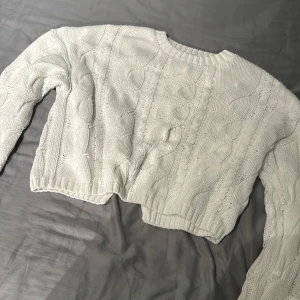 Vit croppad stickad tröja från BikBok - Säljer en vit croppad stickad tröja från BikBok med kabelstickat mönster. Tröjan har lång ärm och rund halsringning, perfekt för lager på lager under kyliga dagar.