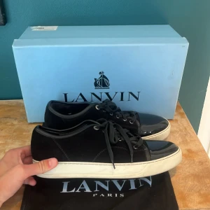 Svarta sneakers från Lanvin med lackad tå - Stilrena svarta sneakers från Lanvin med snygg lackad tå och vit platt sula. Ovandelen är i mocka och skorna har klassisk snörning. Perfekta för dig som gillar en clean och lyxig look med en twist. UK8~43