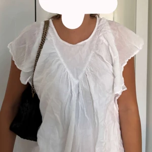 Vit blus med volangärmar - Säljer en luftig vit blus med korta volangärmar och v-ringad effekt framtill. Blusen har en avslappnad passform och är tillverkad i ett tunt, lätt tyg som ger en somrig känsla. Perfekt för dig som gillar en romantisk och enkel stil.