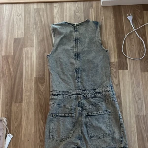 Ärmlös jeansklänning i grå denim - Cool ärmlös jeansklänning i gråtvättad denim med raka linjer och markerade sömmar. Klänningen har rund halsringning, dragkedja bak och stora bakfickor. Perfekt för dig som gillar en avslappnad men edgy stil. Orginal prisen är 399 säljer för 250