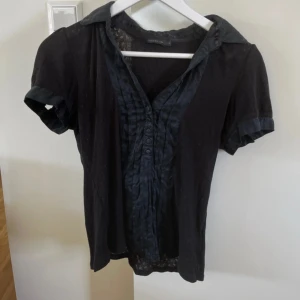 Svart gullig mönstrad blus - Svart gullig mönstrad blus med knappar. Blusen är i strl M och kommer från ”STOCKHOLM”. Mycket bra skick!