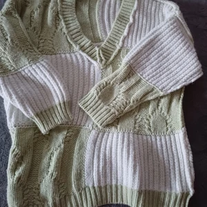 Stickad v-ringad tröja i grönt och vitt - Mysig stickad tröja med v-ringning i blockmönster av ljusgrön och vit. Tröjan har grov ribbstickning blandat med flätstickade partier och långa ärmar. Perfekt för dig som gillar en chill och trendig look.