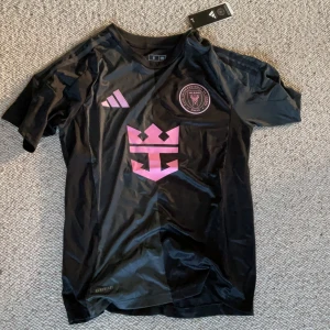 Inter Miami CF svart matchtröja Adidas S - Snygg svart Inter Miami CF fotbollströja från Adidas i slim fit. Tröjan har korta ärmar, rosa klubbmärke och logga på bröstet samt Aeroready-material som andas. Perfekt för dig som vill sticka ut på planen eller läktaren.