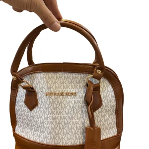 Michael Kors handväska i brunt och vitt - Snygg handväska . Väskan har bruna skinnhandtag och detaljer, rundad form och guldfärgade metalldetaljer. Perfekt storlek för det viktigaste och stängs med dragkedja upptill.