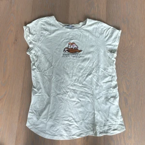 Mint grön t-shirt med tryck från FB Siser - Mint grön t-shirt från FB Siser i bomull med ett gulligt tryck av sengångare, katt och koala samt texten 'Just Chill...'. Klassisk rund hals och korta ärmar. Perfekt för dig som gillar chill vibes och söta motiv.