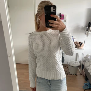 Vit stickad tröja med strukturmönster - Säljer en vit stickad tröja med snyggt strukturmönster och ribbade muddar vid ärmslut och nederkant. Tröjan har rund halsringning och lång ärm, perfekt att matcha med jeans eller kjol för en clean och fräsch look.