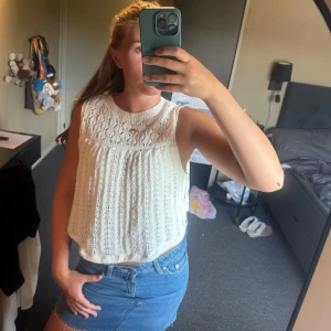 Vit stickad ärmlös topp från Zara - Supersöt vit stickad topp från Zara med ärmlös design och rund hals. Toppen har ett fint hålmönster och är croppad, perfekt till jeans eller kjol. Materialet är mjukt och luftigt, vilket gör den skön att bära under varma dagar.
