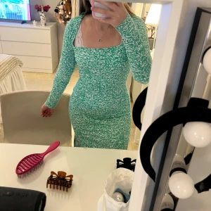 Grönmönstrad långklänning med långa ärmar - Snygg långklänning i grönt och vitt med mönster, figurnära passform och långa ärmar. Klänningen har fyrkantig ringning och är perfekt för dig som gillar en trendig och bekväm stil. Materialet känns stretchigt och mjukt mot huden.