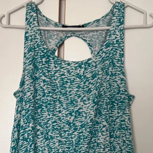 Grönvit mönstrad kortklänning - Snygg kortklänning från Gina Tricot i vitt och grönt med abstrakt mönster. Ärmlös modell med rund hals och cool cut-out detalj i ryggen. Klänningen har en lätt utställd kjol och resår i midjan för skön passform. Perfekt för varma dagar!